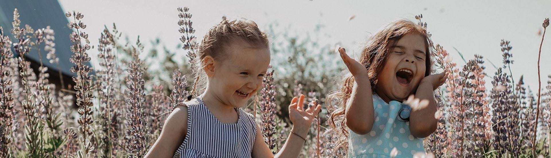 To små piger står på en blomstereng er griner hjerteligt og ser ud til at hygge sig meget.