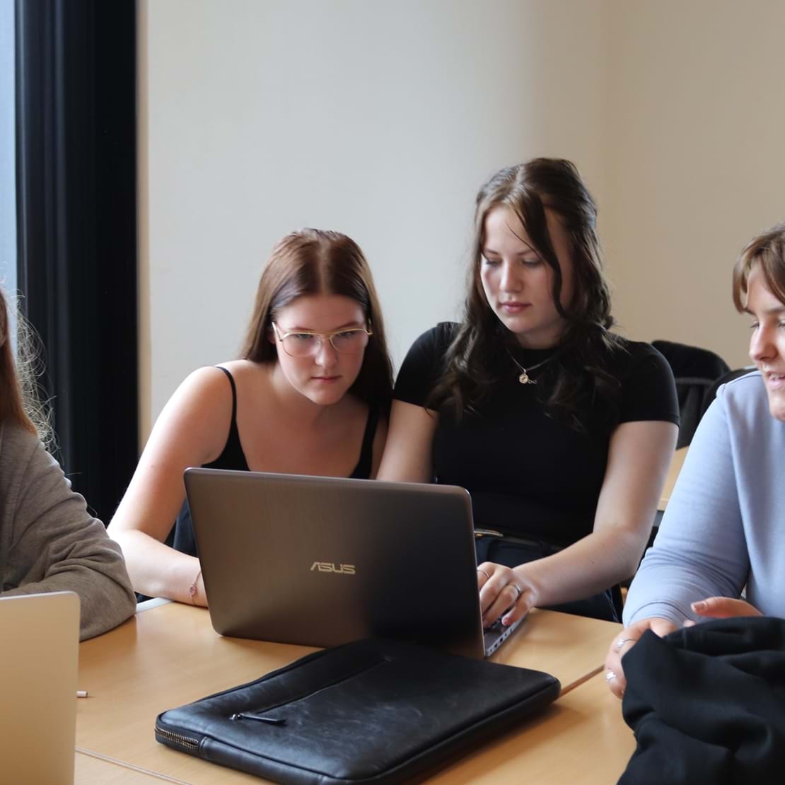 Fire unge elever sidder i en gruppe og kigger ind i en laptop, imens de debatterer det der er på skærmen.