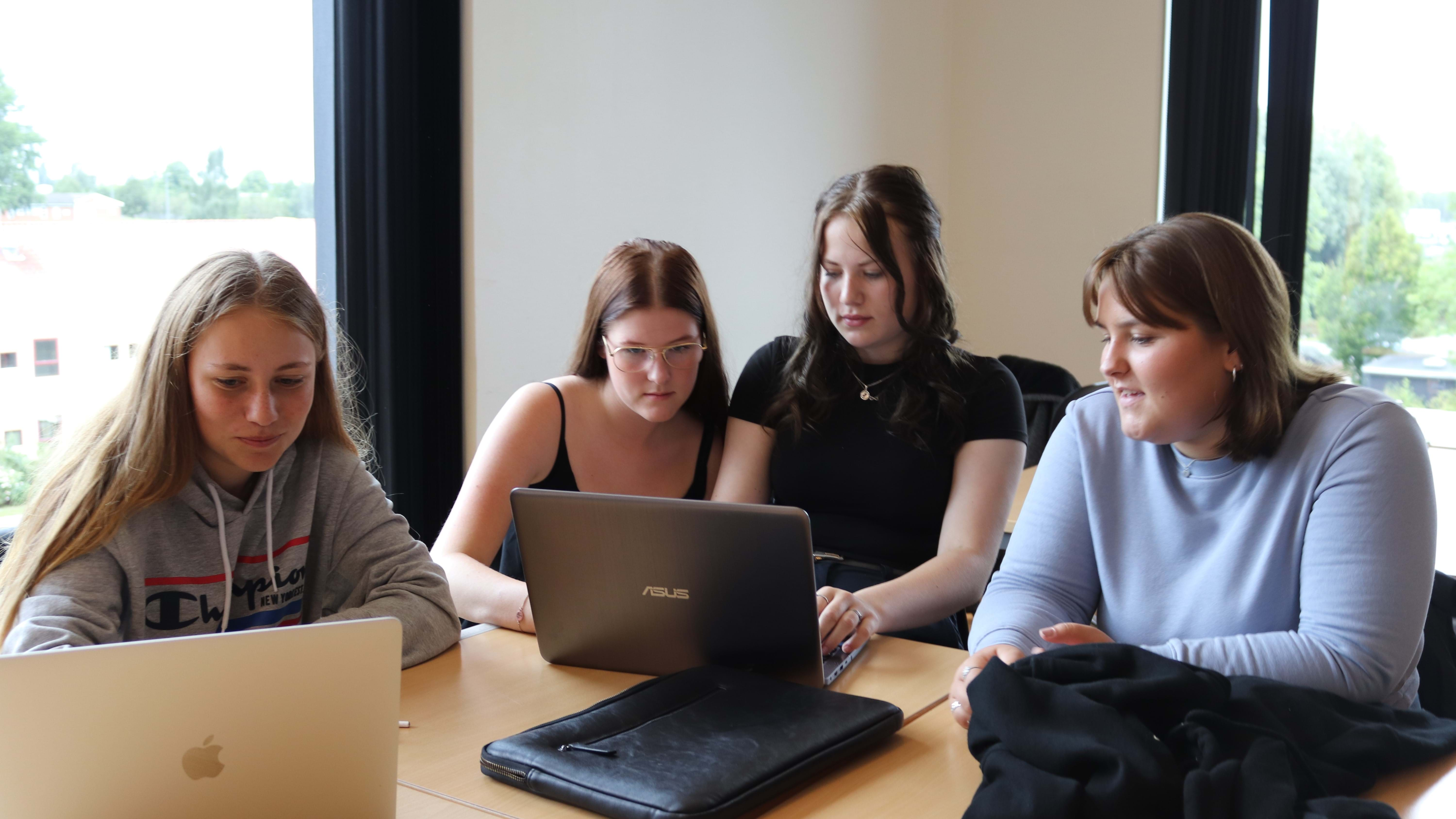 Fire unge elever sidder i en gruppe og kigger ind i en laptop, imens de debatterer det der er på skærmen.