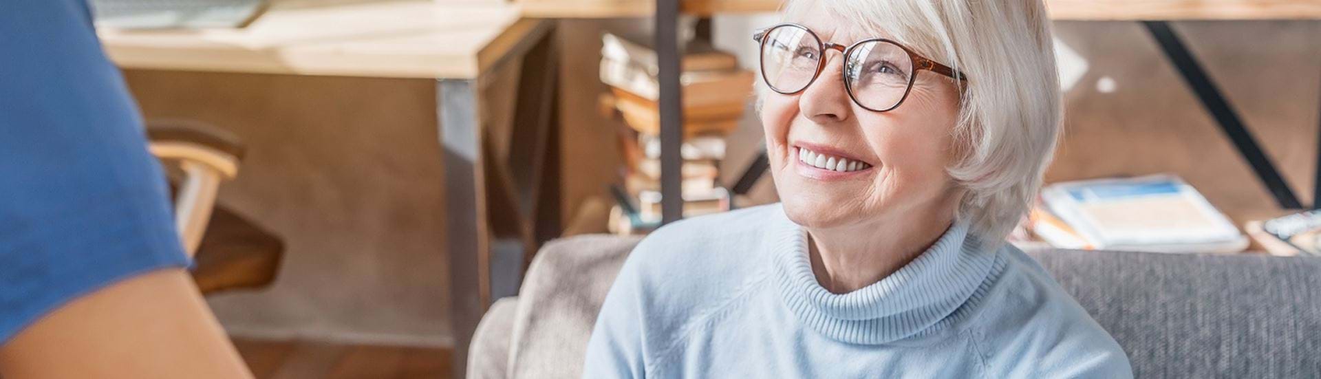 En ældre dame kigger spilende op på en uniformeret person, som holder hende i hænderne.