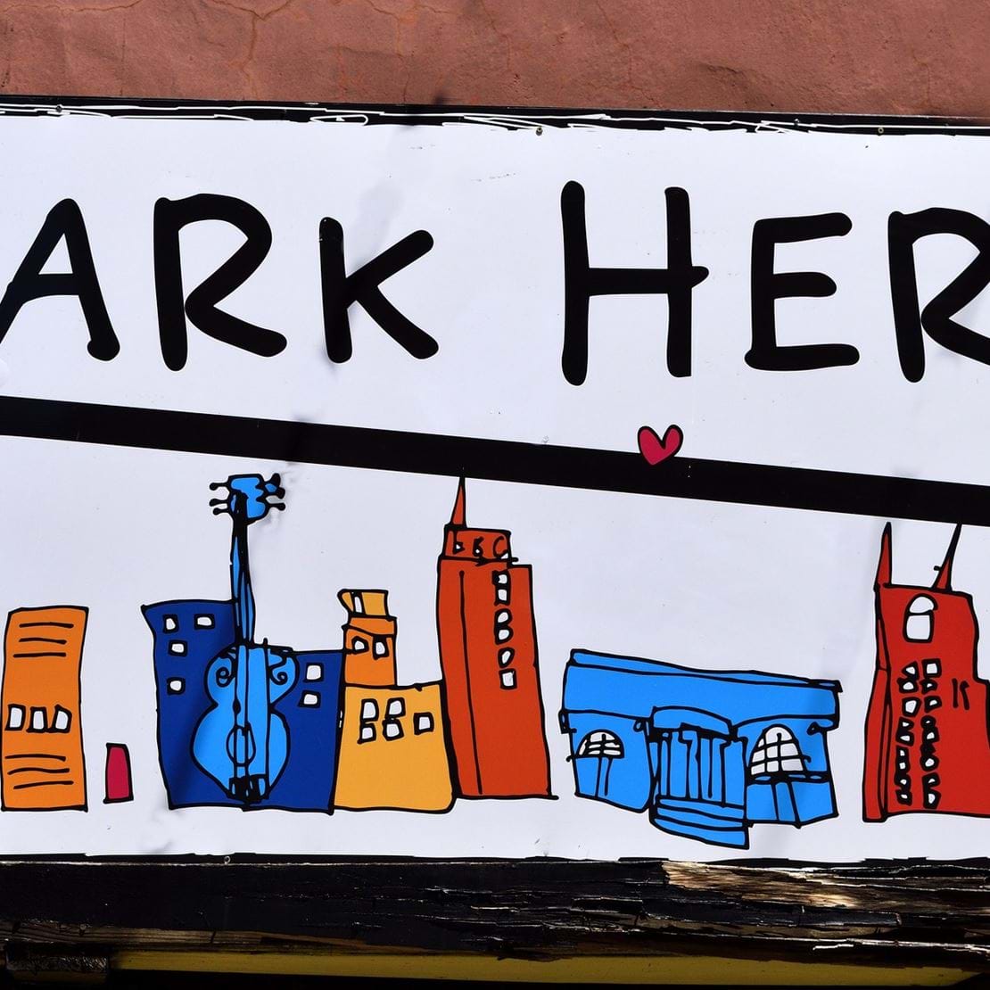 Et skilt med en illustraton af en storby med højhuse og skriften "park here!".