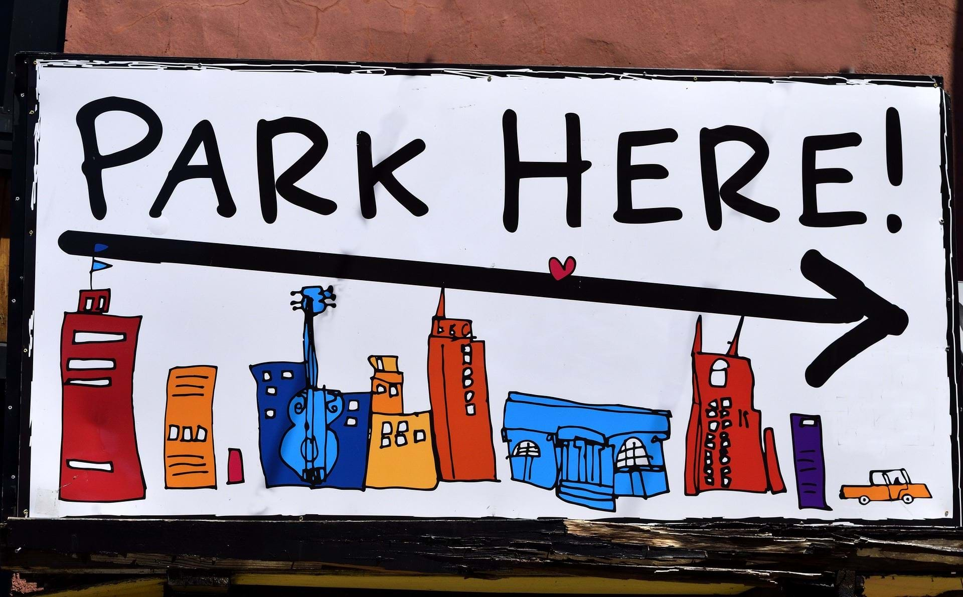 Et skilt med en illustraton af en storby med højhuse og skriften "park here!".