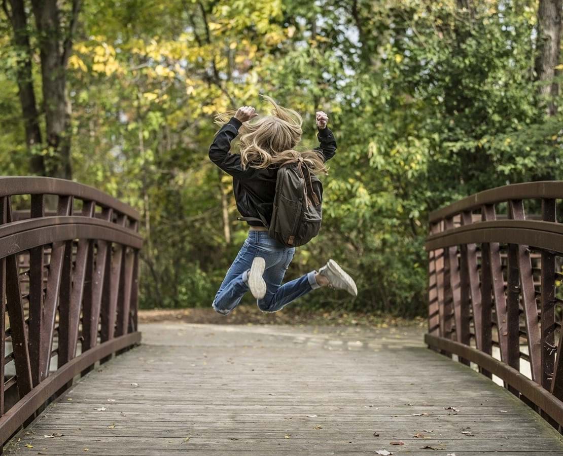 Skolepige hopper i jubel midt på en træbro
