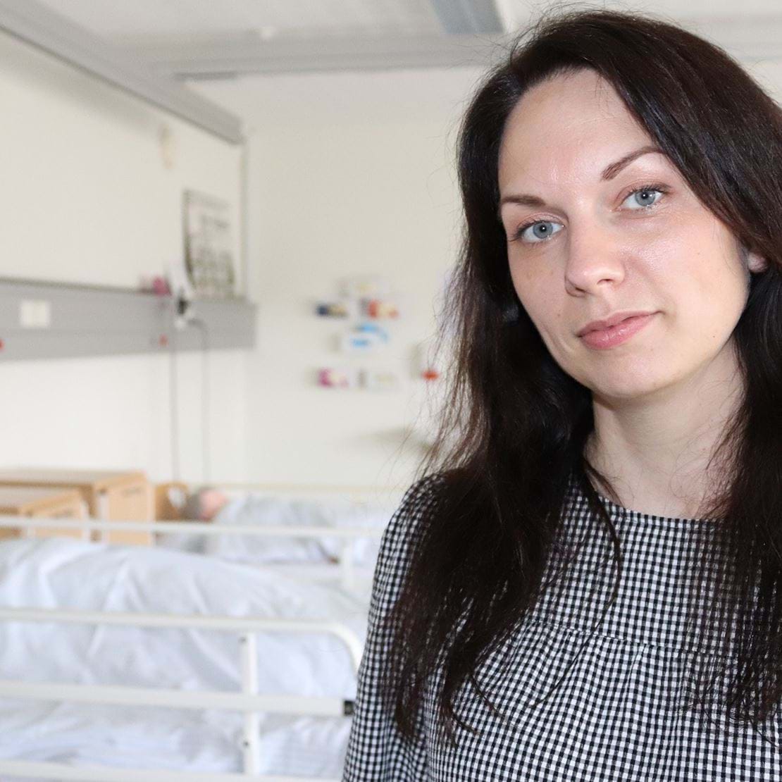 Billede af Monika Mattox der kigger smilende ind i kameraet. Bag hende står senge som på en hospitalsstue.