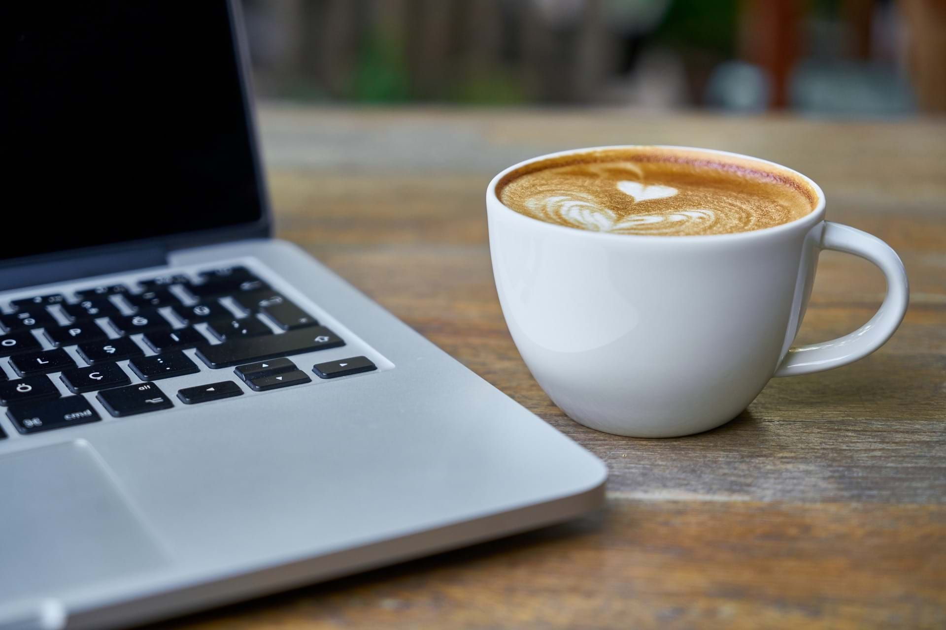 En kop cappucino med hjerte i mælkeskummet og en laptop ved siden af.