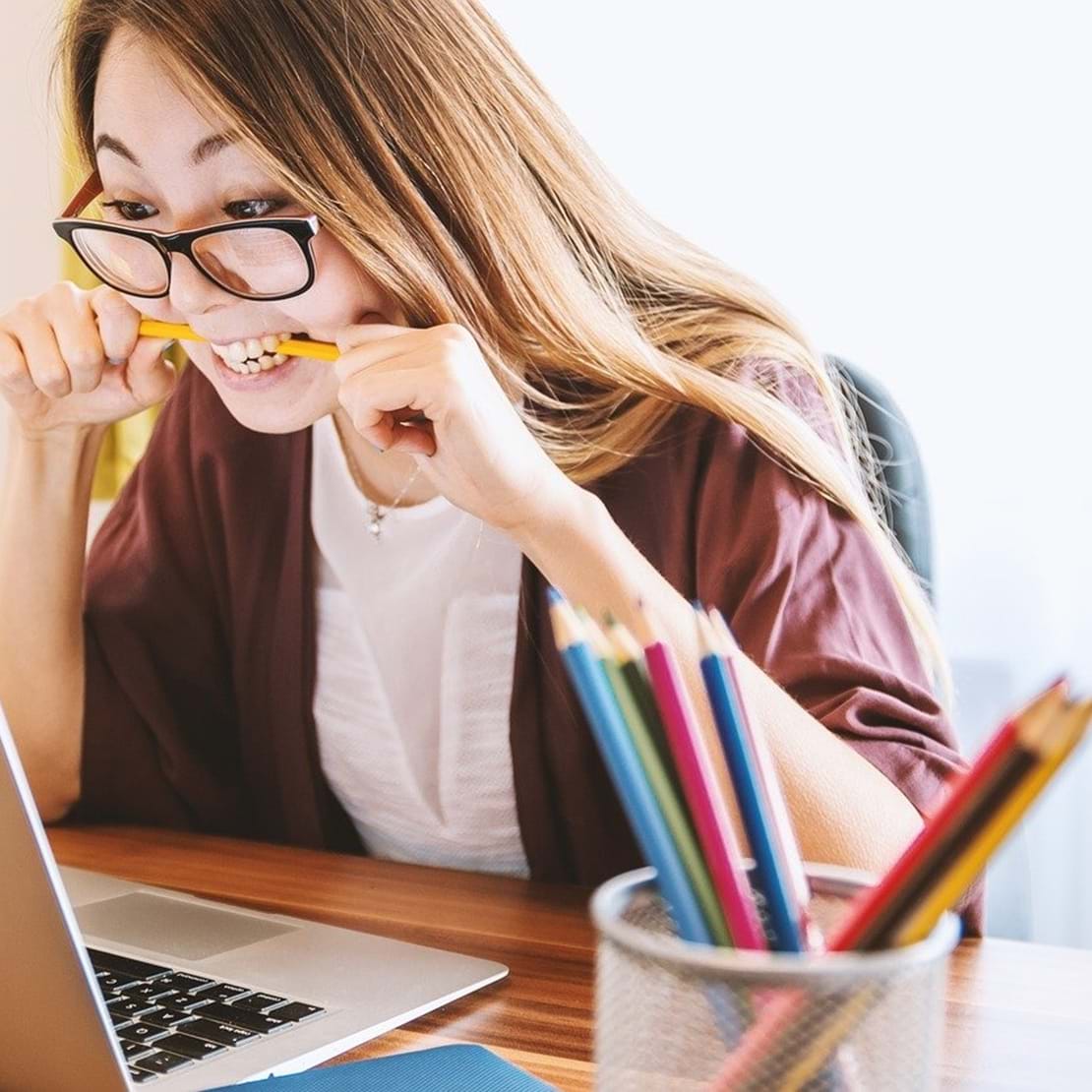 Ung, kvindelig studerende bider i sin blyant i frustration imens hun stirrer ind i skærmen på sin laptop.