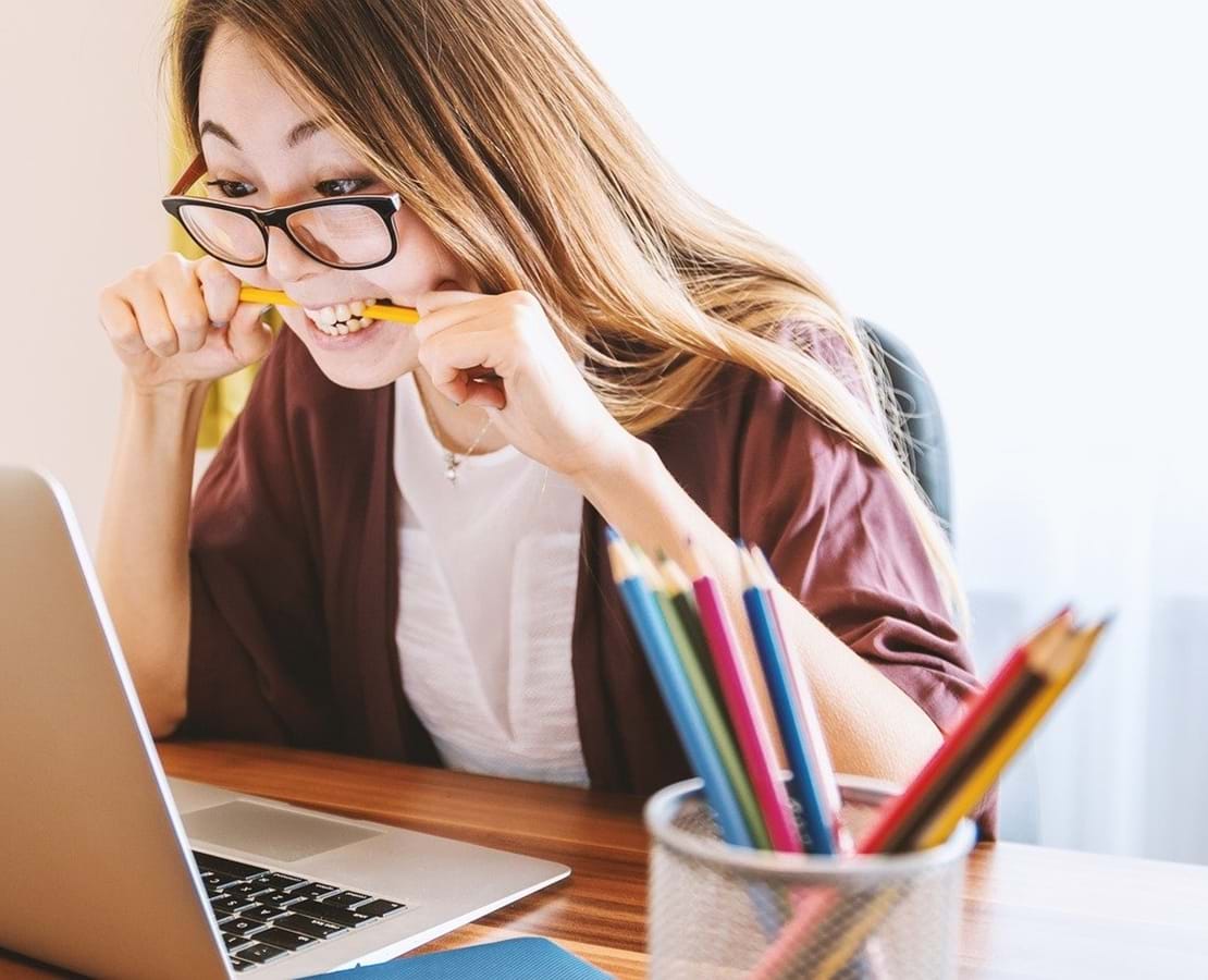 Ung, kvindelig studerende bider i sin blyant i frustration imens hun stirrer ind i skærmen på sin laptop.