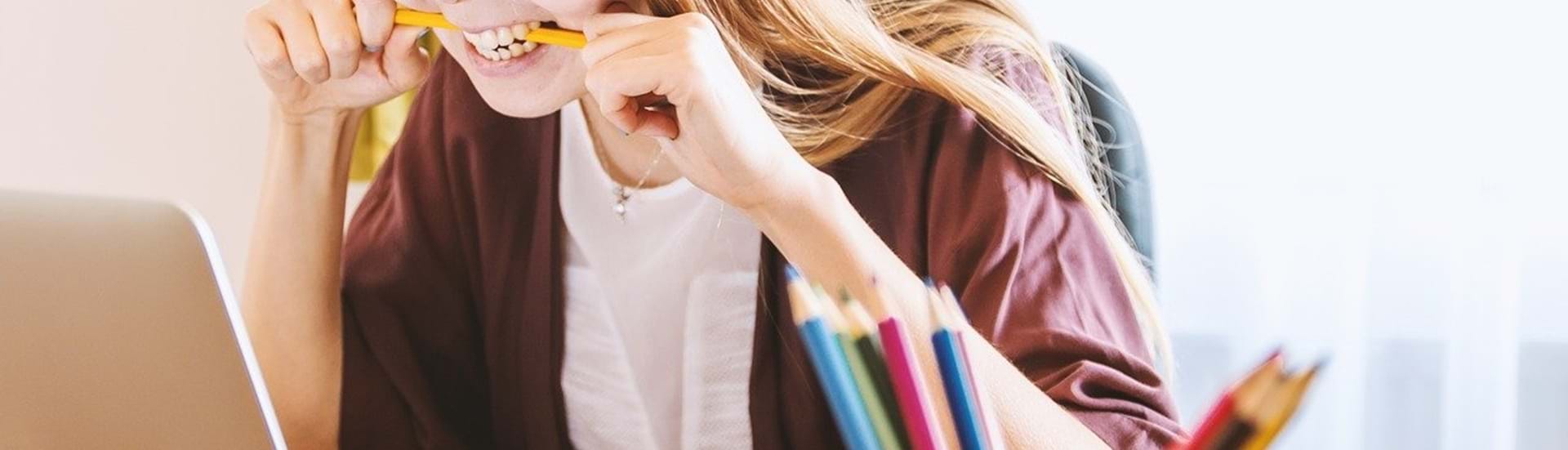 Ung, kvindelig studerende bider i sin blyant og kigger frustreret ind i skærmen på sin laptop