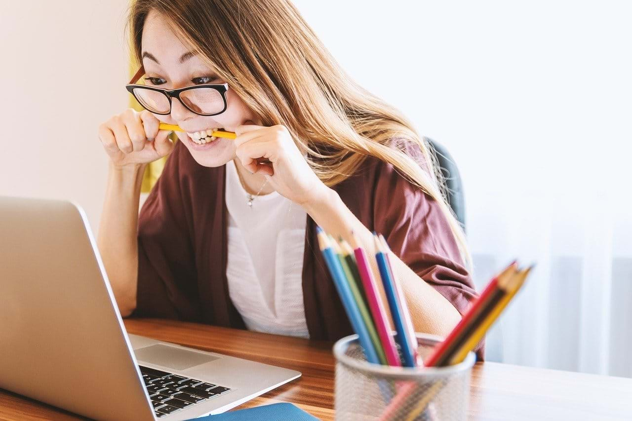 Ung, kvindelig studerende bider i sin blyant i frustration imens hun stirrer ind i skærmen på sin laptop.