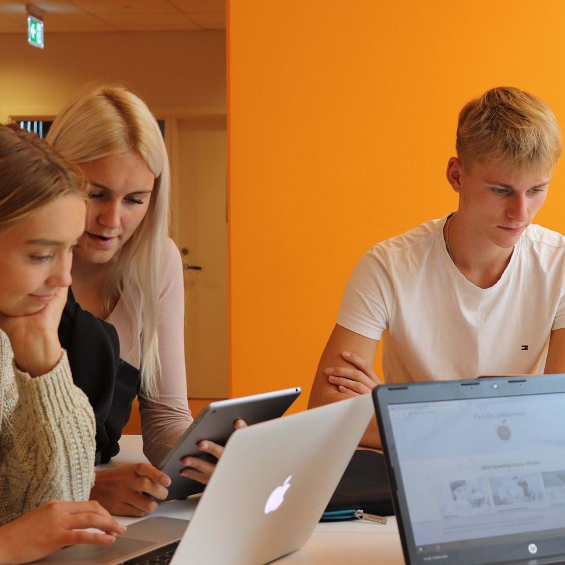 Tre unge elever sidder i gruppearbejde og kigger sammen på en computer.