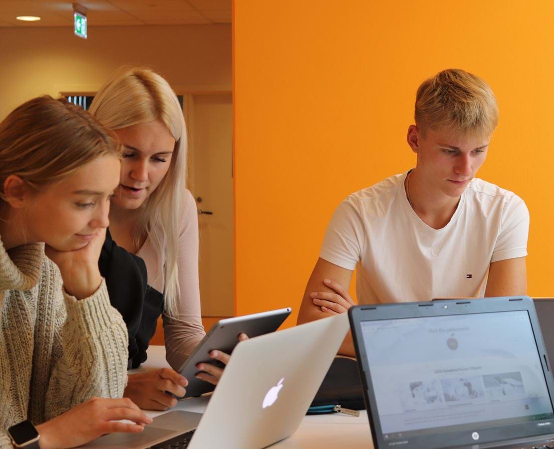 Tre unge elever sidder i gruppearbejde og kigger sammen på en computer.