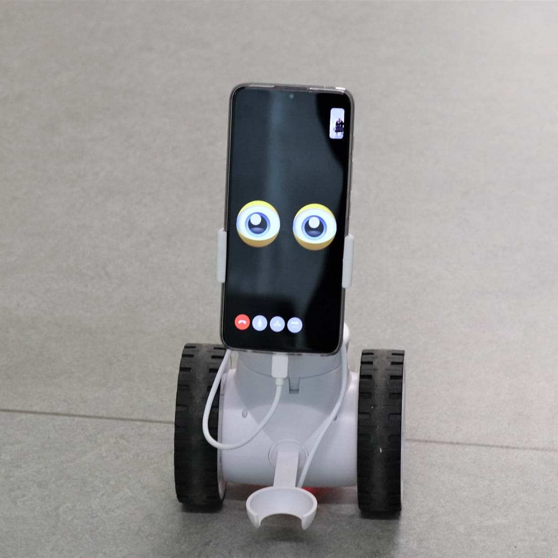 En lille robot med hjul på kigger ind i kameraet med sine tegnede øjne.