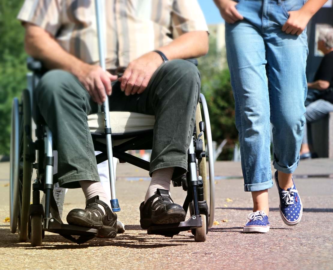 Social- og sundhedshjælper går tur sammen med en ældre mand i kørestol