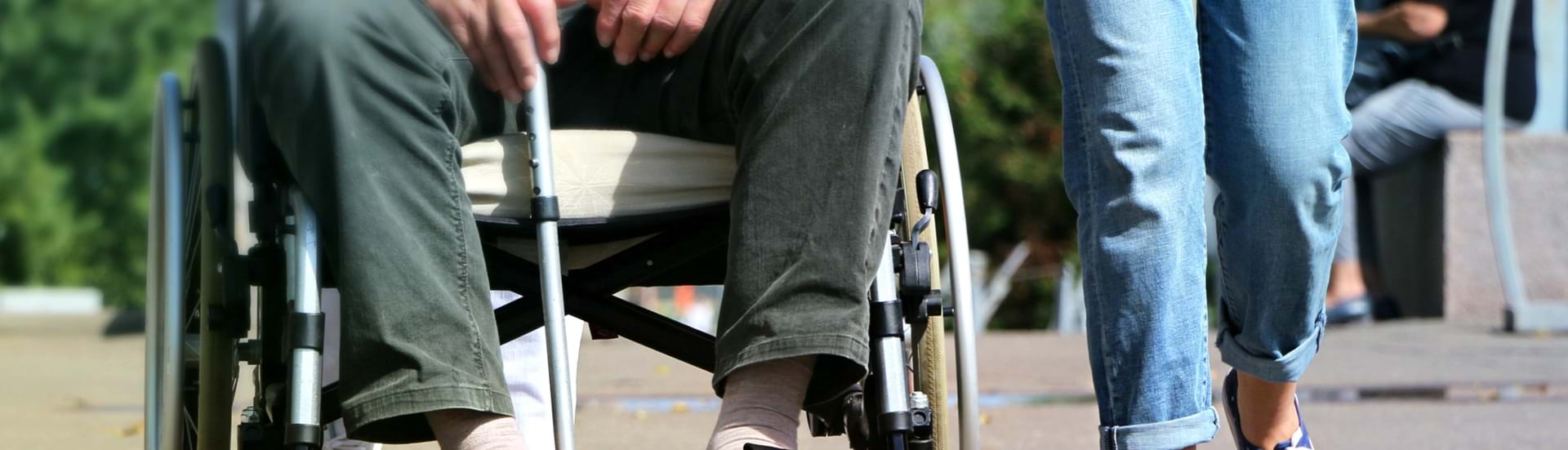 Social- og sundhedshjælper der går tur sammen med en ældre mand i kørestol