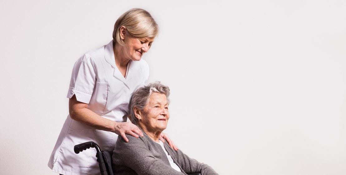 Social- og sundhedshjælper sammen med en ældre kvinde i kørestol.