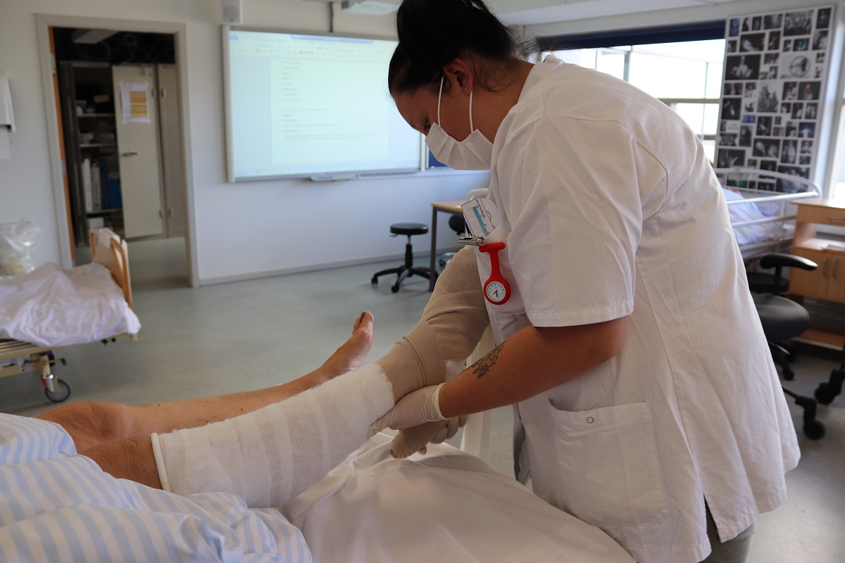 Social- og sundhedsassistent sætter støttestrømpe på et ben.