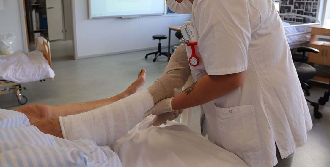 Social- og sundhedsassistent sætter støttestrømpe på et ben.