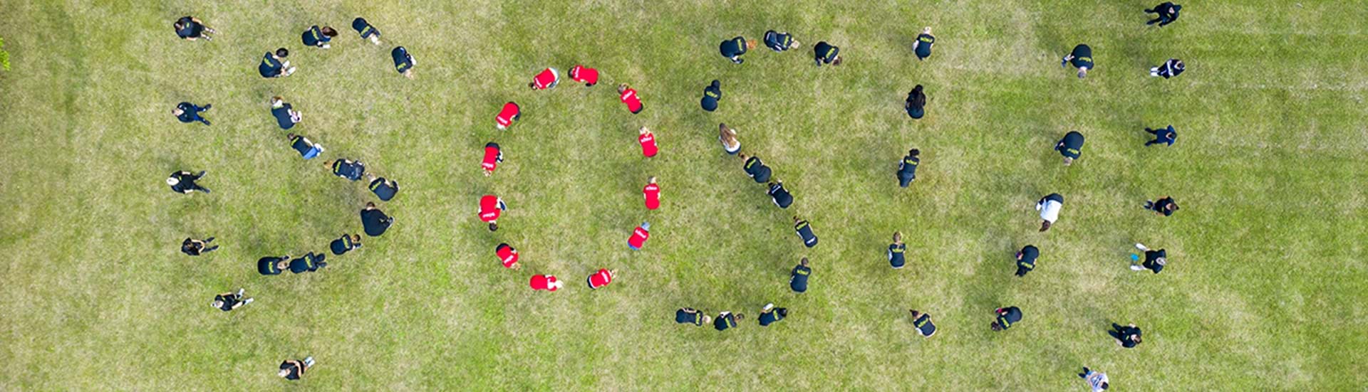 SOSU stavet med elever på en stor græsplæne og fotograferet fra oven. 