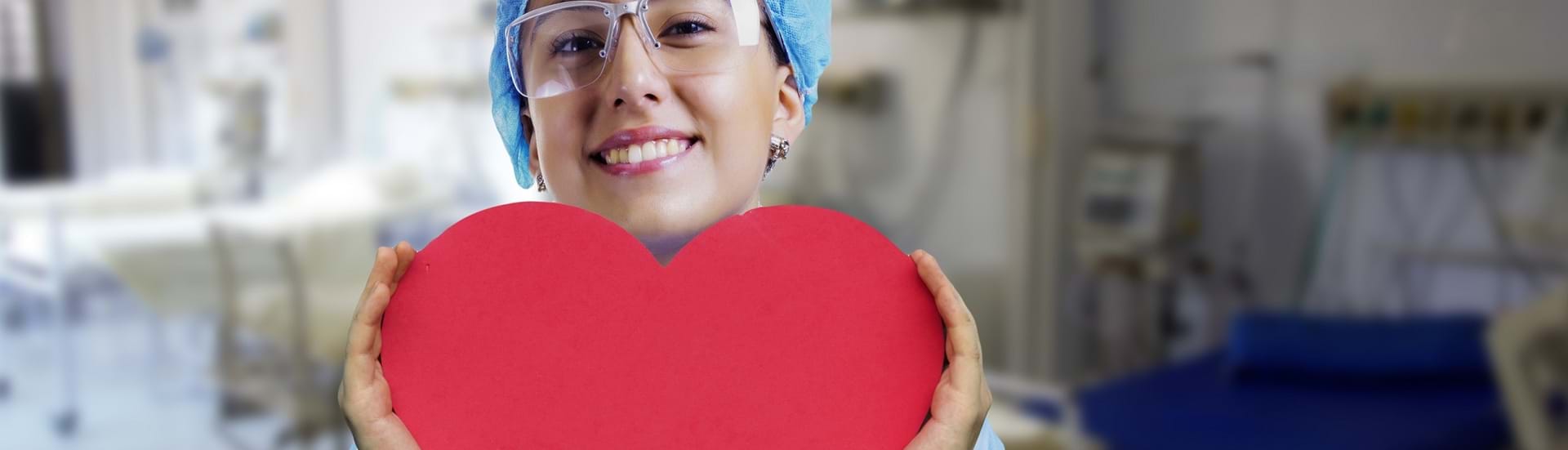 Ung pige i sygeplejeuniform holder et rødt hjerte i hænderne og smiler ind i kameraet.