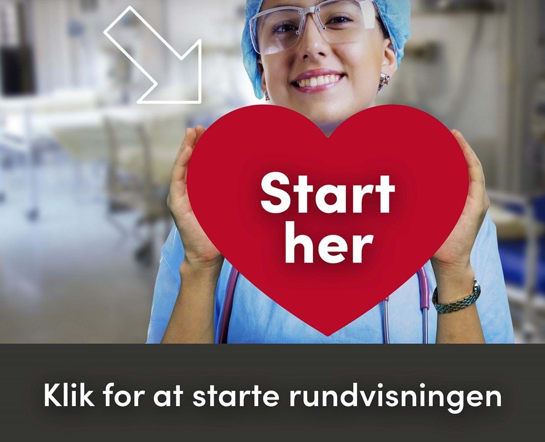Ung kvinde i blå sygeplejeuniform holder et stort, rødt hjerte foran sig og smiler til kameraet.