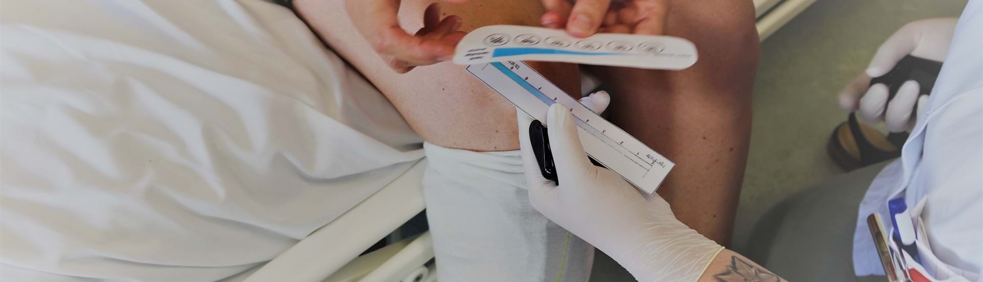 En social- og sundhedsassistentelev hjælper en patient med at lokalisere hvor ondt hun har ved at tale med hende ud fra en smerteskala.